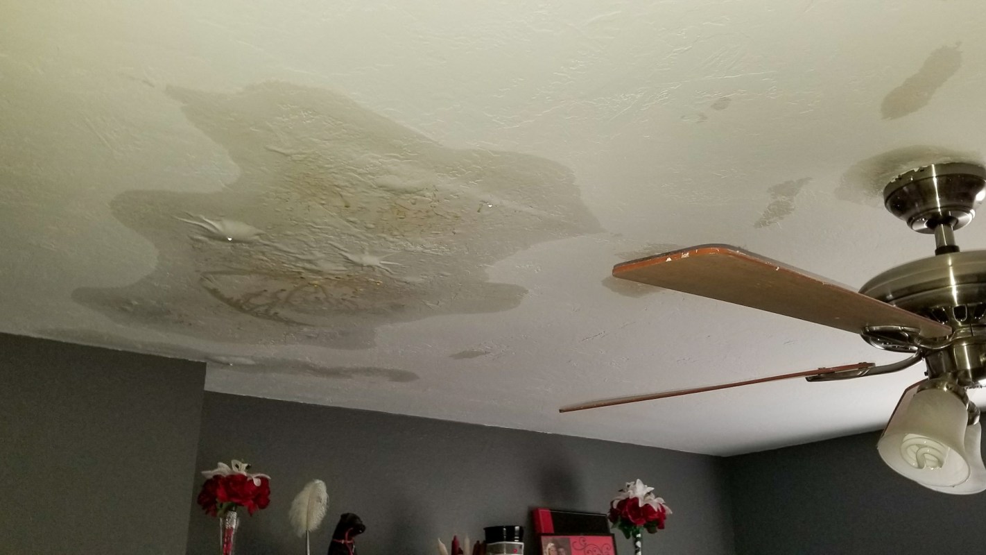 Water damage is visible on the ceiling, with stains and a ceiling fan in the room.