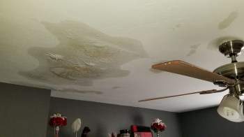 Water damage is visible on the ceiling, with stains and a ceiling fan in the room.