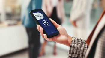 A person holds a smartphone displaying a travel insurance app in a busy setting.