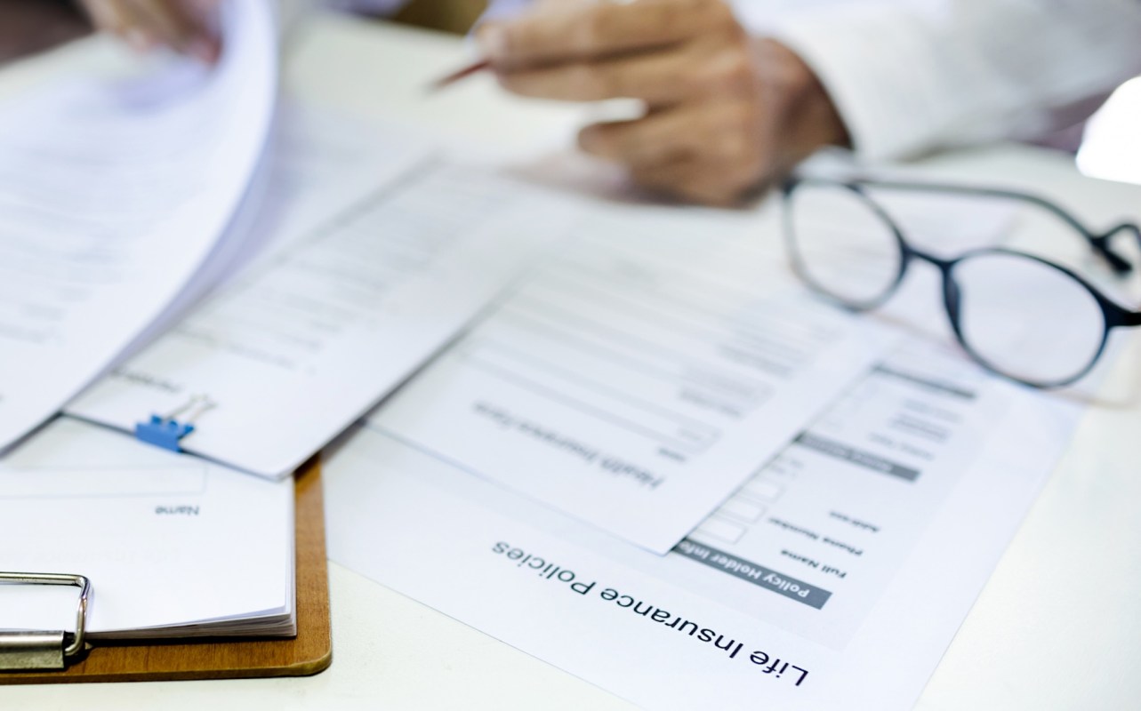 Papers and a pair of glasses are on a table, with documents related to life insurance policies visible.