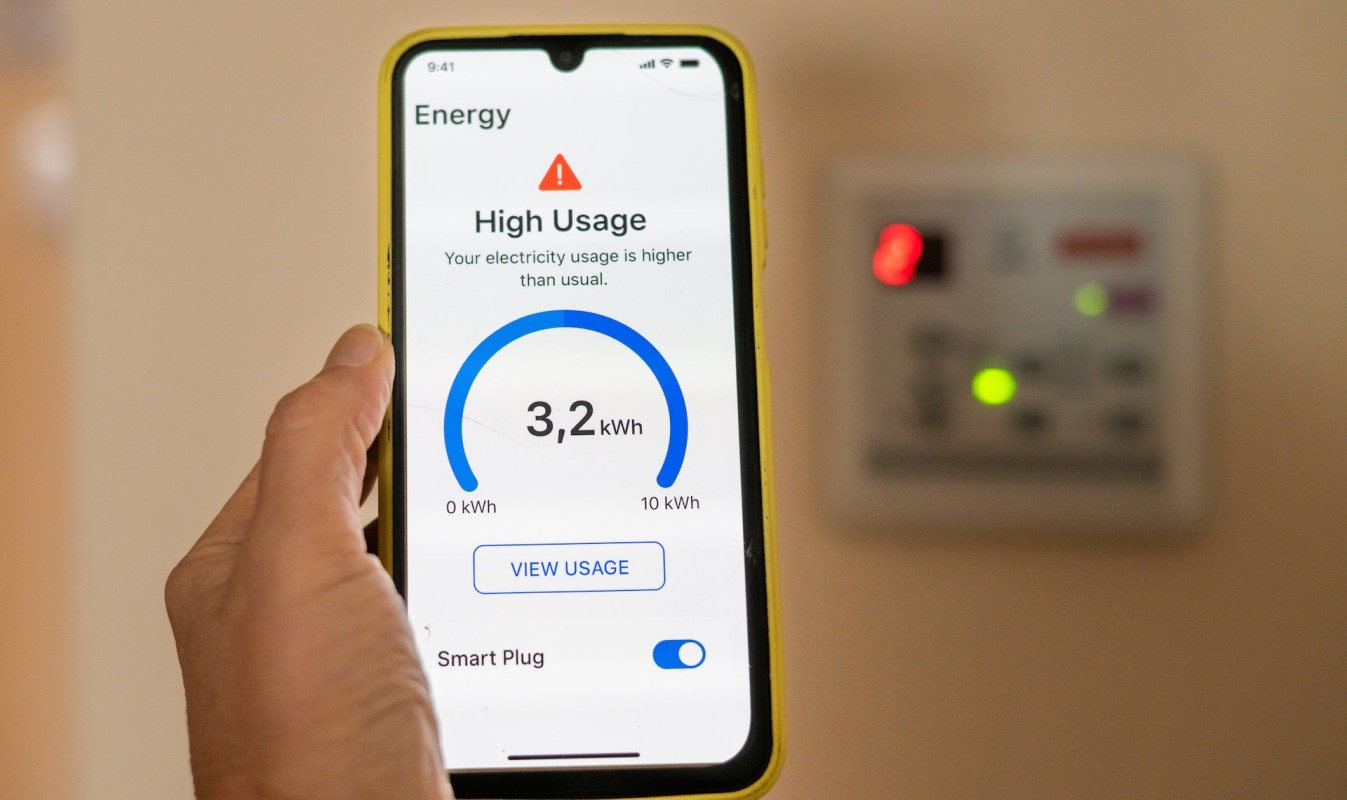A person holds a smartphone displaying an energy usage alert and statistics.