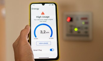 A person holds a smartphone displaying an energy usage alert and statistics.