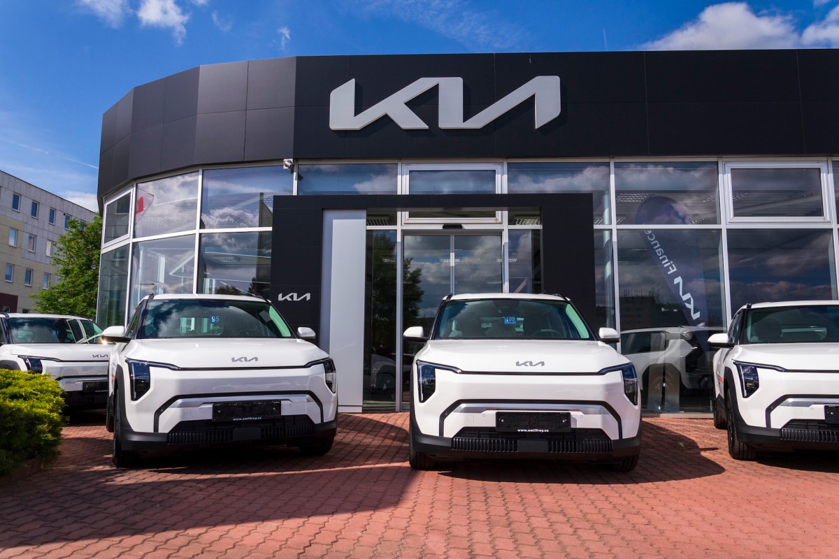 A Kia car dealership with several white vehicles parked in front of a modern building.