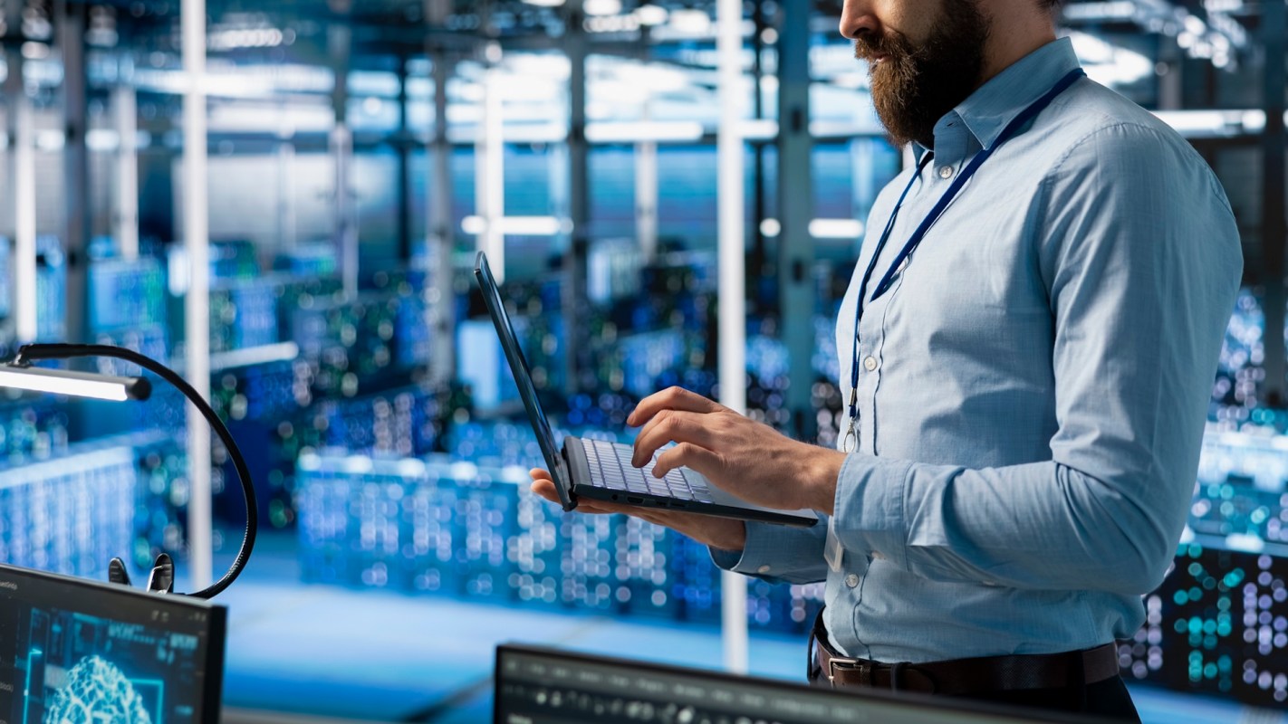 A man uses a laptop in a data center.