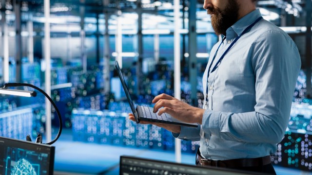 A man uses a laptop in a data center.