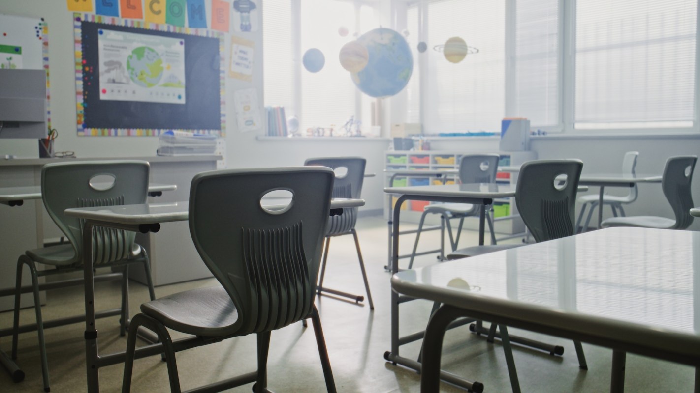 An empty classroom with desks, chairs, and a blackboard displaying educational materials.
