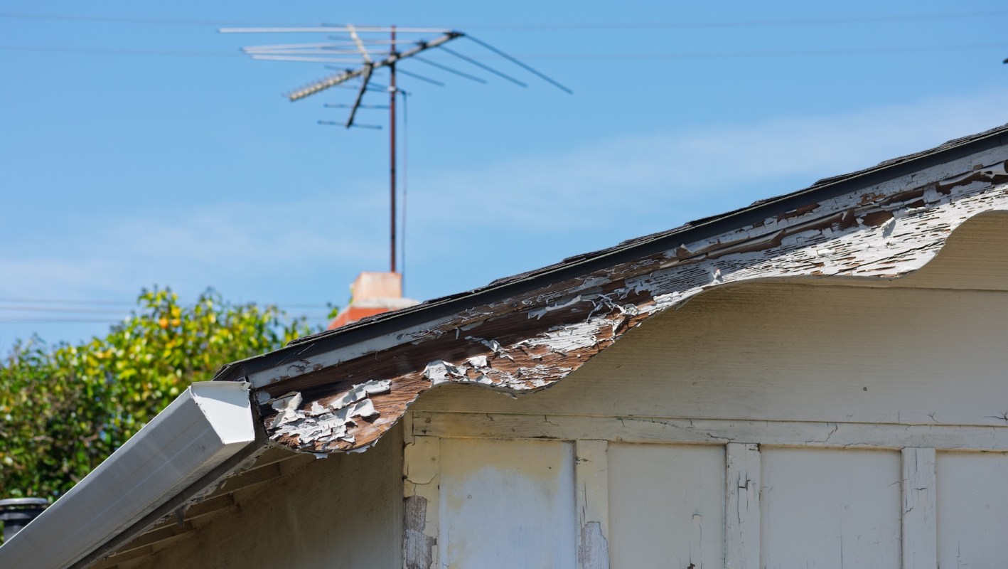 A building with peeling paint on the eaves and an antenna visible against a blue sky.