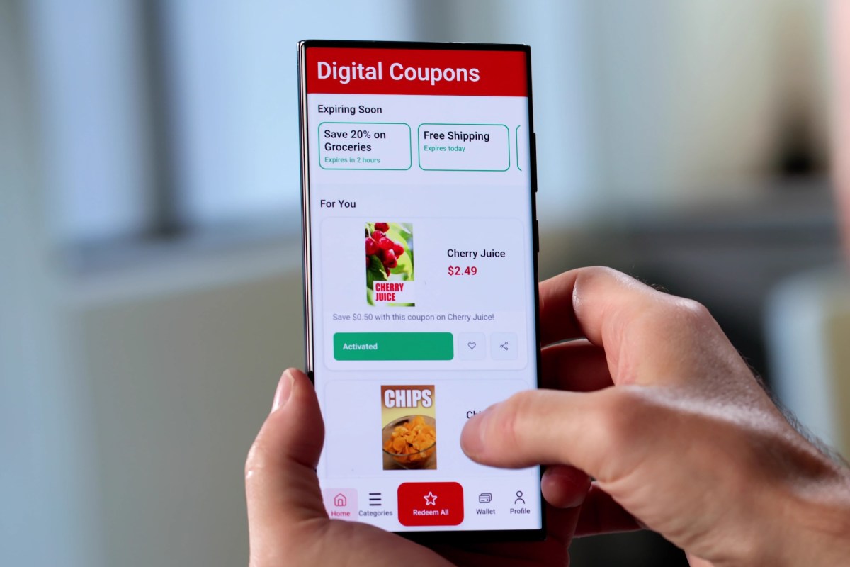 A person interacts with a smartphone displaying a digital coupon app featuring offers for groceries.
