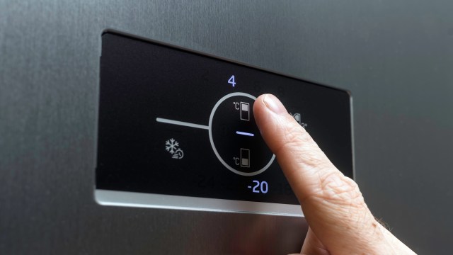 A finger touching a control panel on a freezer.