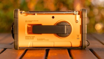 An orange digital receiver with a retractable hand crank, along with various controls and indicators, on a wooden surface.