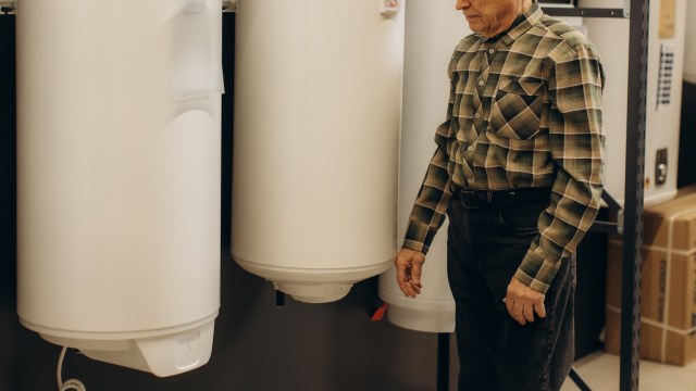 A man stands next to several water heaters in a store setting.