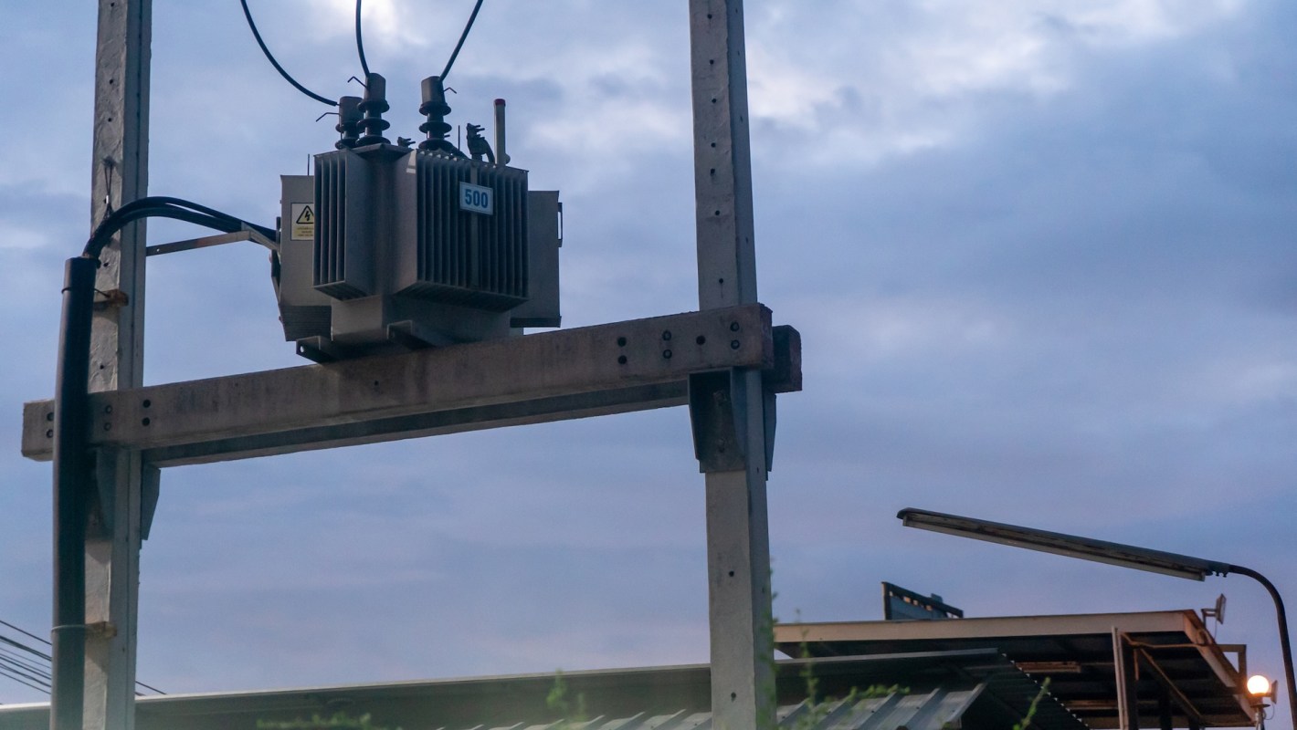 A power transformer mounted on a utility pole against a cloudy sky.