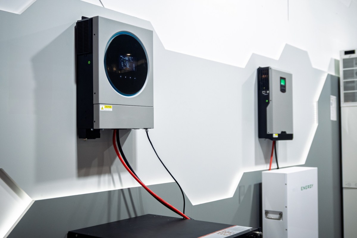 Two battery inverters mounted on a wall, with wires connected to a black device on the floor.