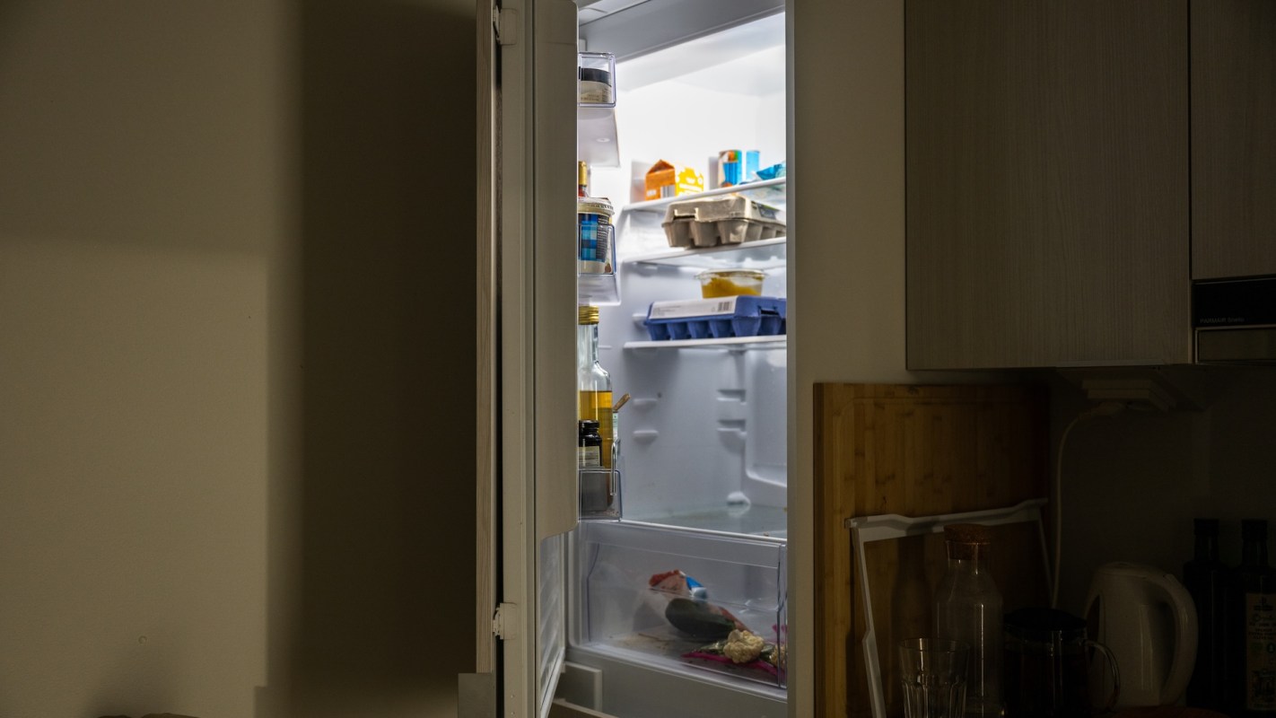 A refrigerator filled with various food items and containers, partially open in a kitchen setting.