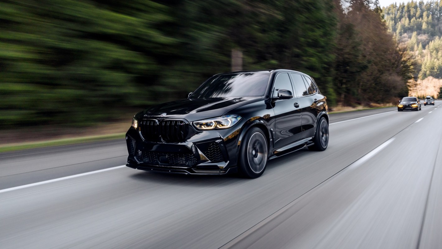 A black BMW X5 SUV drives on a highway surrounded by trees.