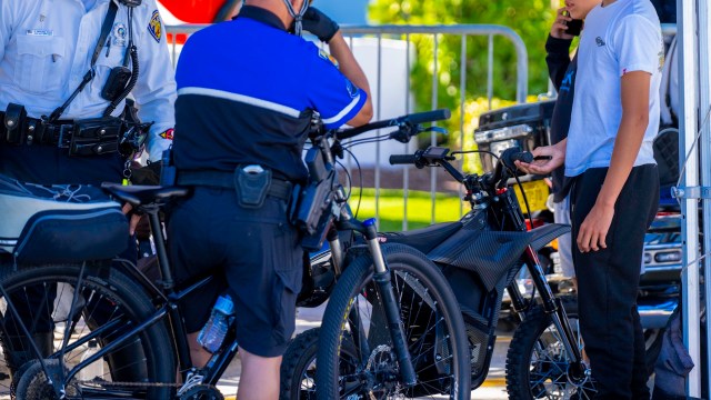 Two police officers interact with a young man near e-bicycles at an outdoor event.