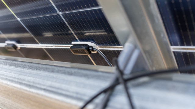 A solar panel with connecting wires and a junction box mounted on a metal frame.