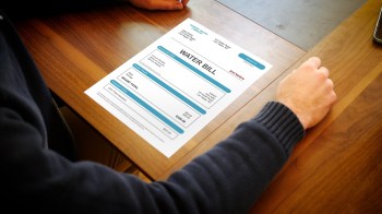 A person reviews a water bill on a wooden table.