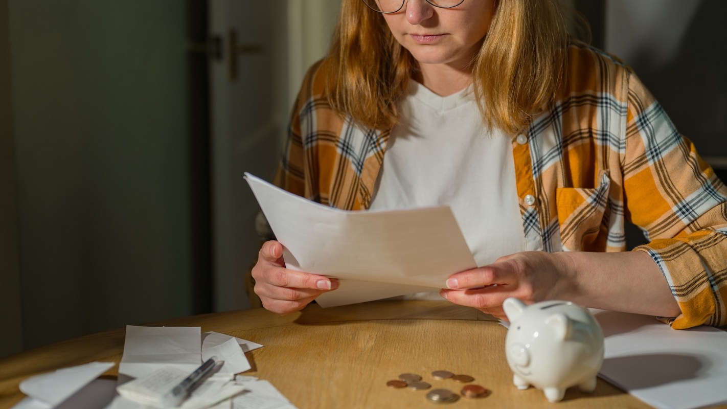 A person reviews documents at a table with coins and a piggy bank.