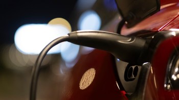 An electric vehicle charging cable is connected to a charging port at night.