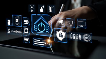A hand holding a stylus interacts with a digital tablet displaying various smart home icons.