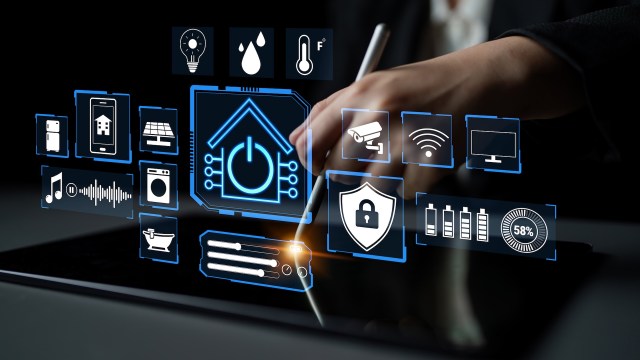 A hand holding a stylus interacts with a digital tablet displaying various smart home icons.