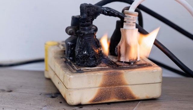 A burned power strip with smoke and flames at the connectors.