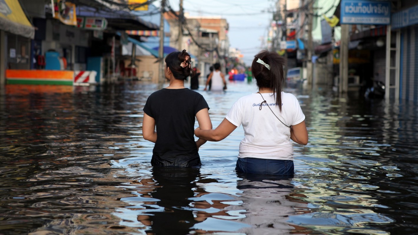 Two women walk hand in hand through a flooded street with water reaching mid-calf.