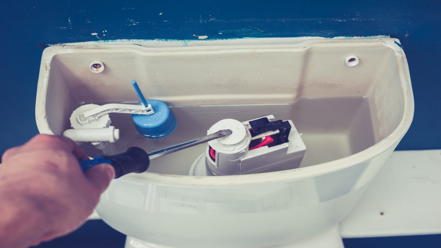 A person uses a screwdriver to repair the inside of a toilet tank.