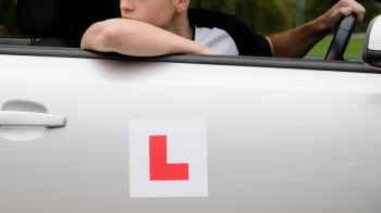 A learner driver rests an arm on a car window.