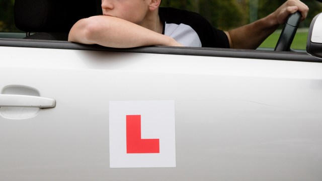 A learner driver rests an arm on a car window.