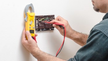 A person using a multimeter to test wiring on a wall-mounted thermostat.