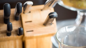 A wooden knife block containing several kitchen knives next to a glass container.
