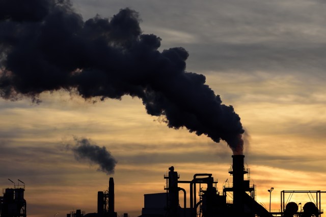 Industrial chimneys releasing smoke at sunset.