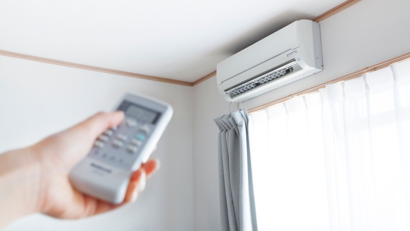 A hand holding a remote control pointed at a mini-split unit on the wall.