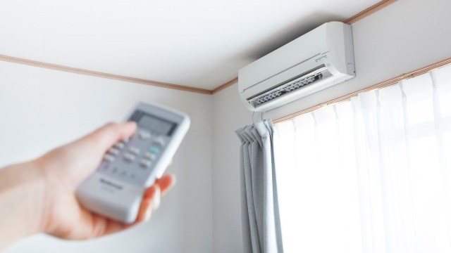 A hand holding a remote control pointed at a mini-split unit on the wall.