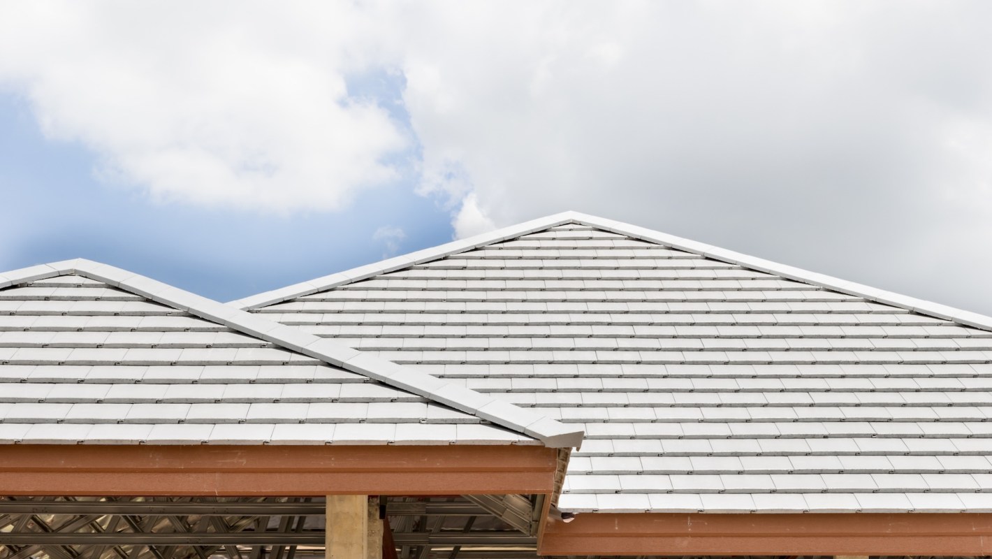 A roof with gray concrete tiles against a partly cloudy sky.