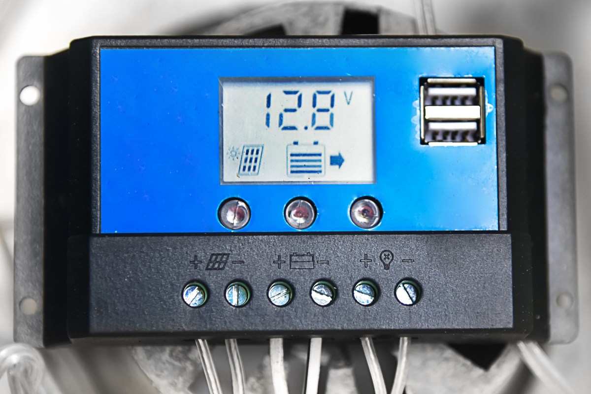 A digital battery monitor displaying a voltage reading of 12.8V with various indicators and connection ports.
