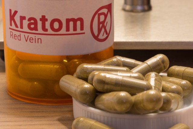 A bottle of "Kratom Red Vein" next to a tray of capsules.