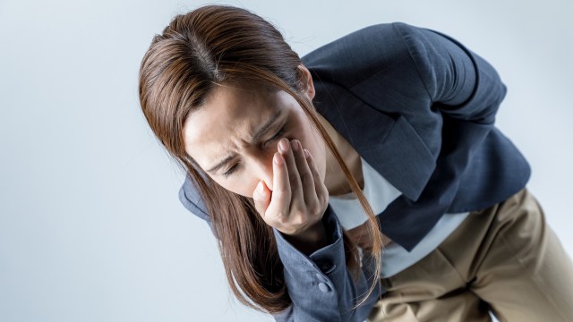 A woman in a business suit bends forward, covering her mouth with one hand.