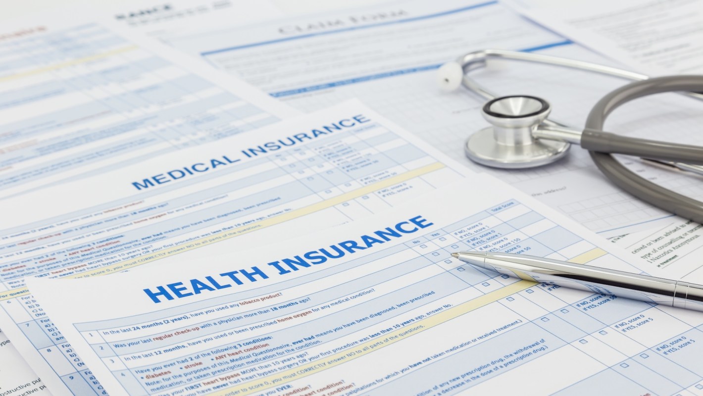 Documents related to health and medical insurance with a stethoscope and a pen on a table.