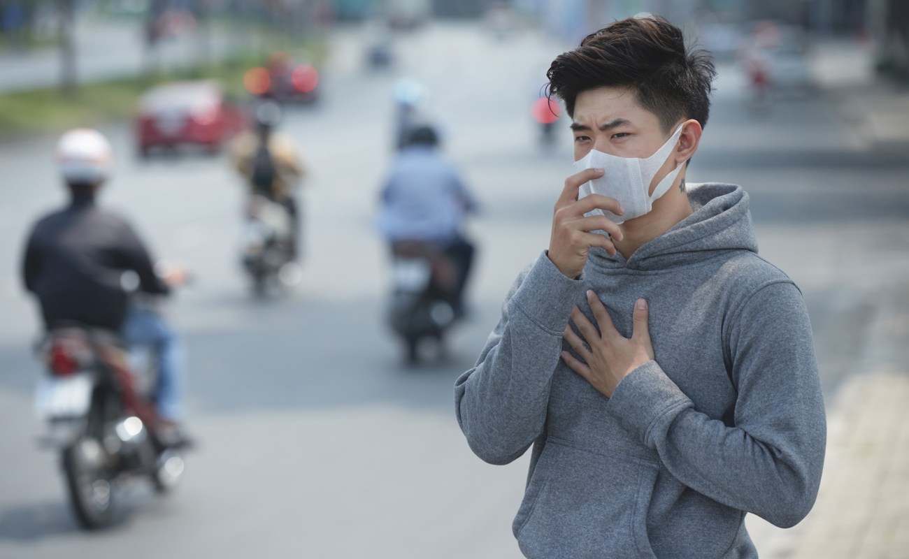 A man wearing a mask by a roadway.