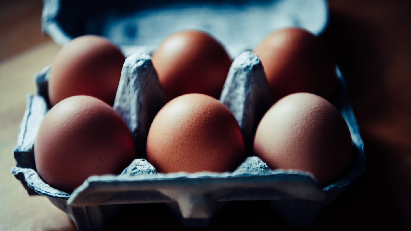 A carton containing six brown eggs on a wooden surface.