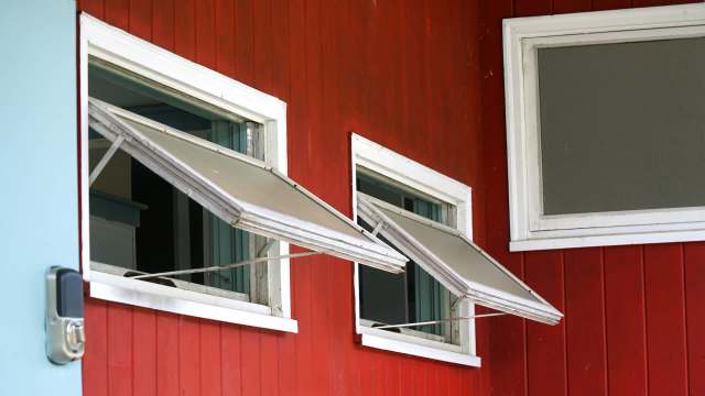 Two open windows with awnings on a red wooden wall.