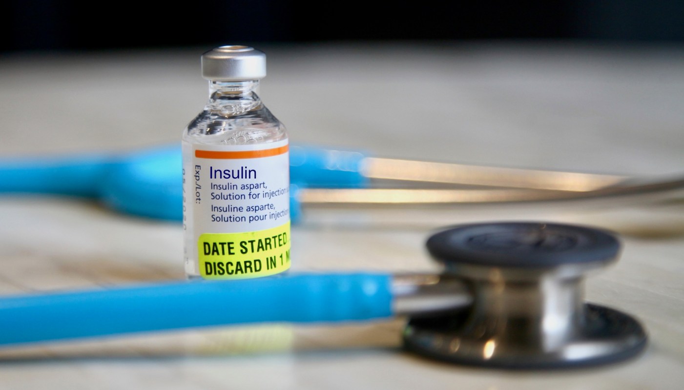 A vial of insulin beside a stethoscope and syringes on a table.