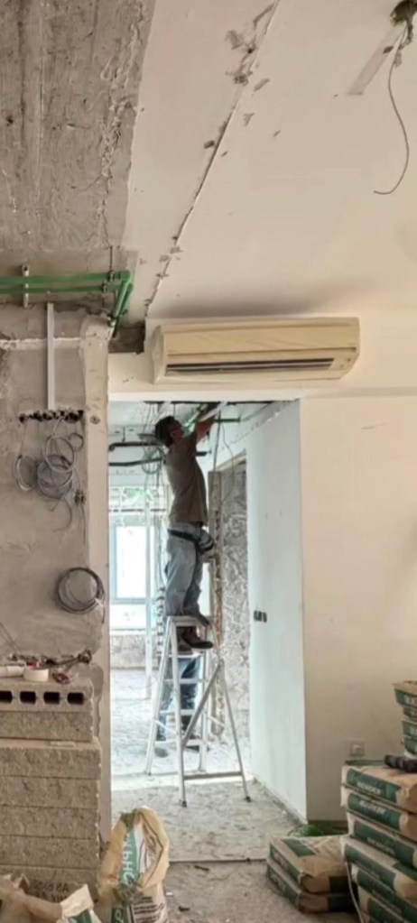 A technician working near a mini-split unit mounted in a tight space.