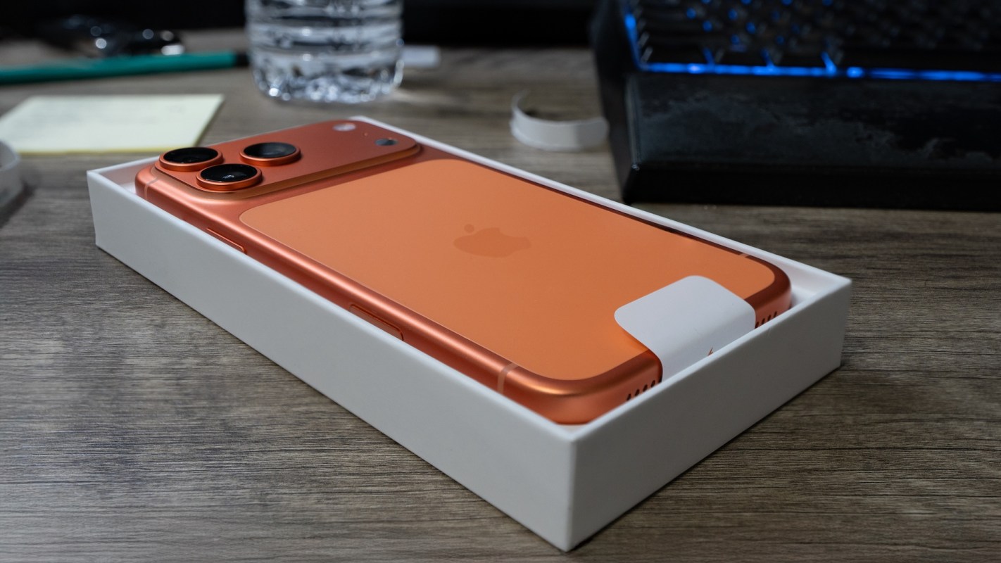 An orange smartphone in its box on a wooden surface.