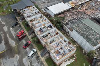 Aerial view of a damaged building from Hurricane Isaias, surrounded by parked cars in a parking lot.