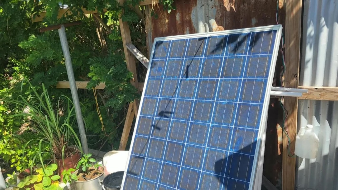 A solar panel next to plants and rustic wooden structures.