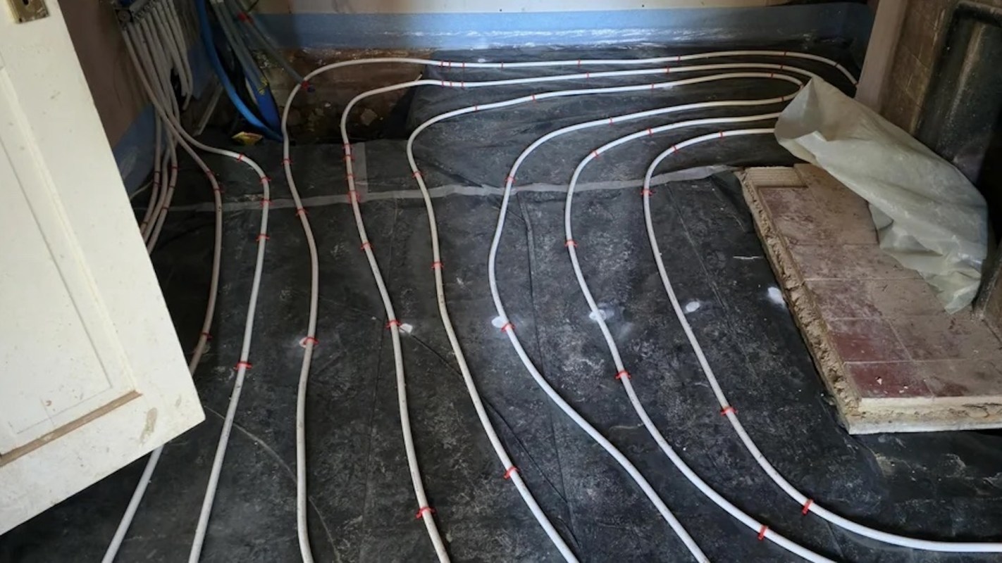 A floor with white pipes arranged on a black surface, some covered with plastic sheeting.